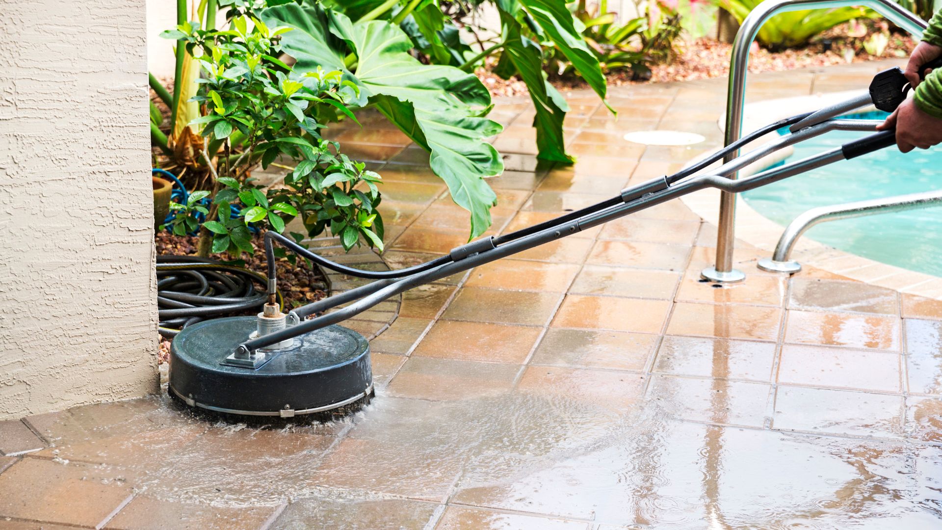 Power washer cleaning tiled patio near plants and swimming pool