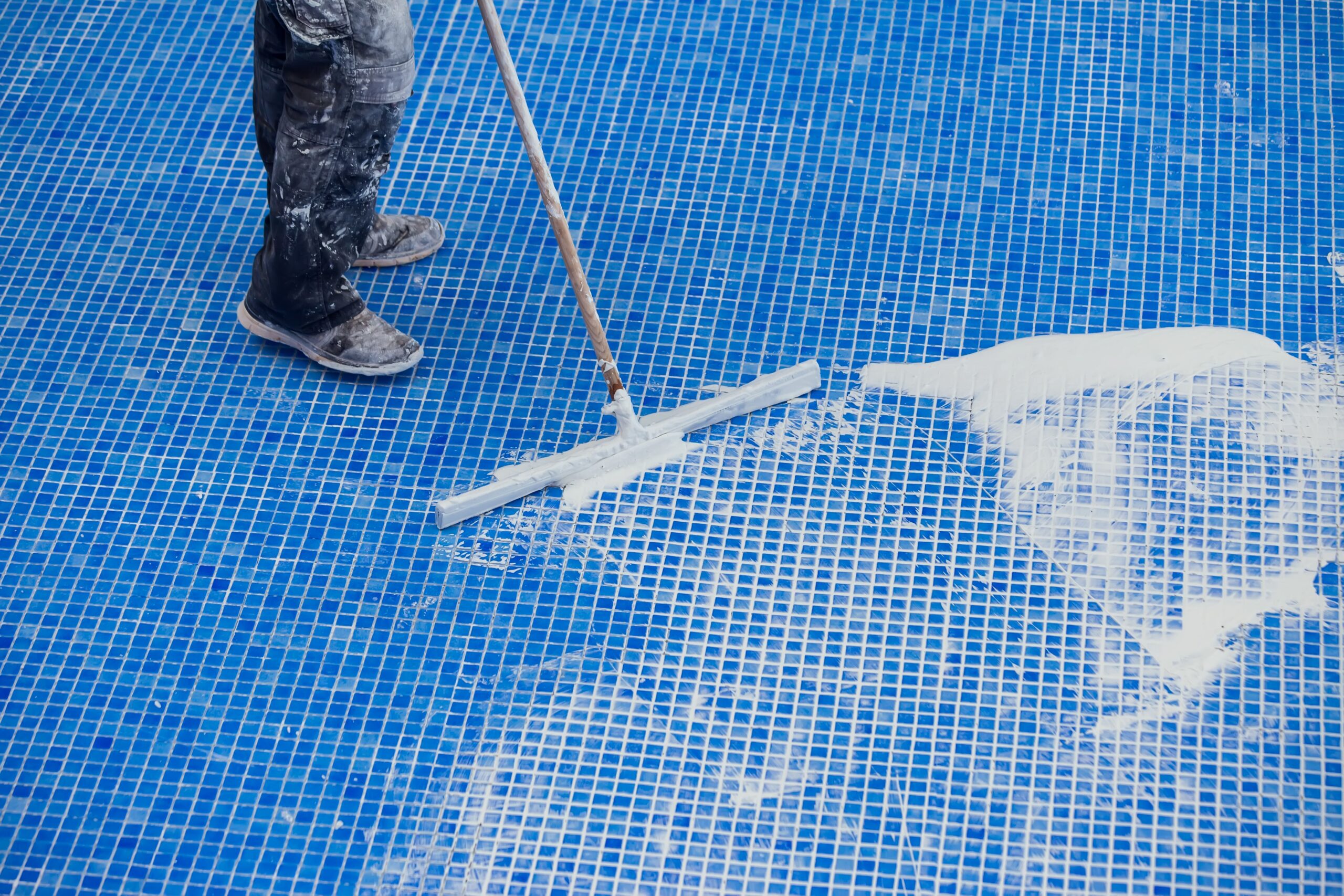 Worker applying white coating on blue tiled surface with squeegee