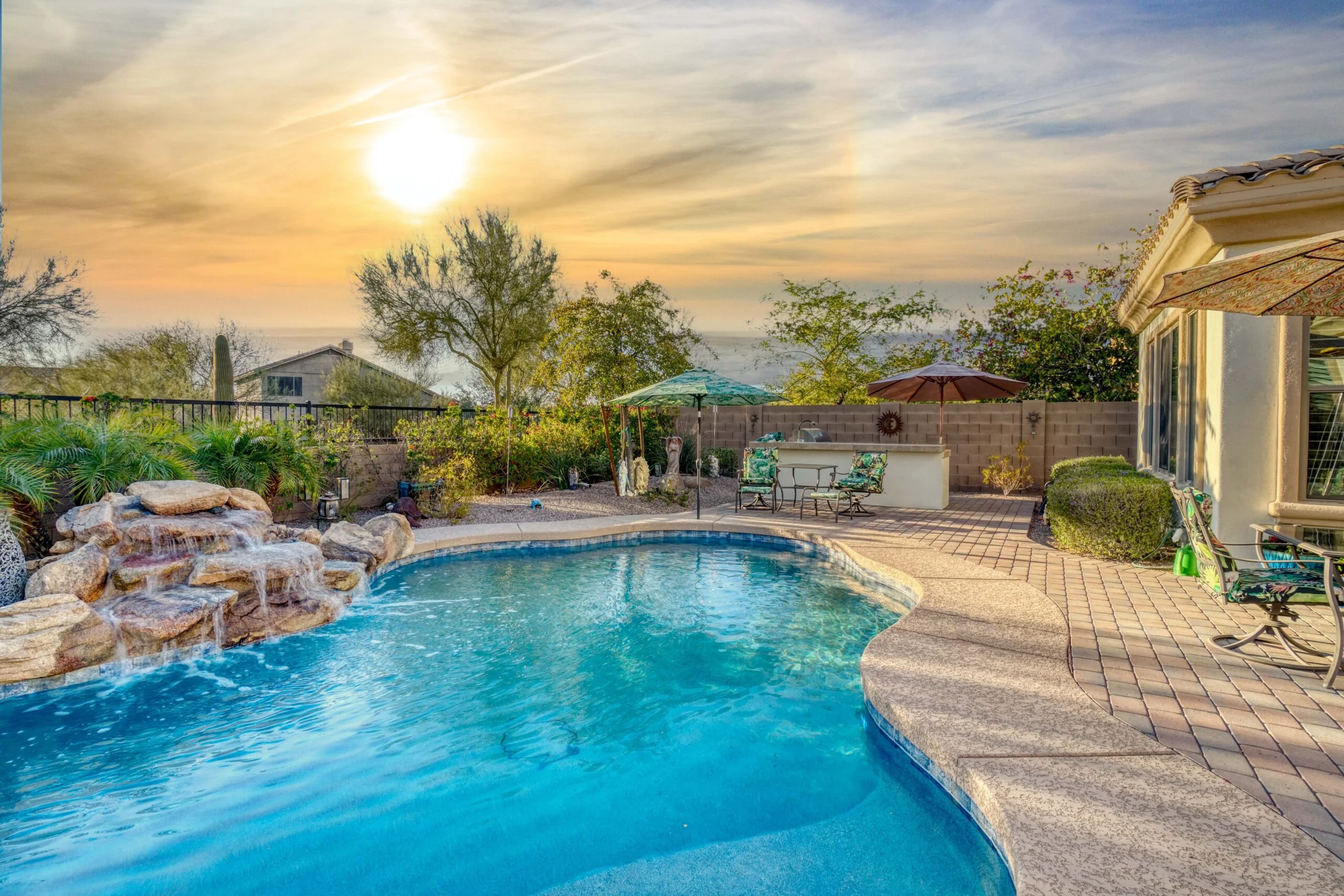 Backyard pool with rock waterfall at sunset in desert landscape